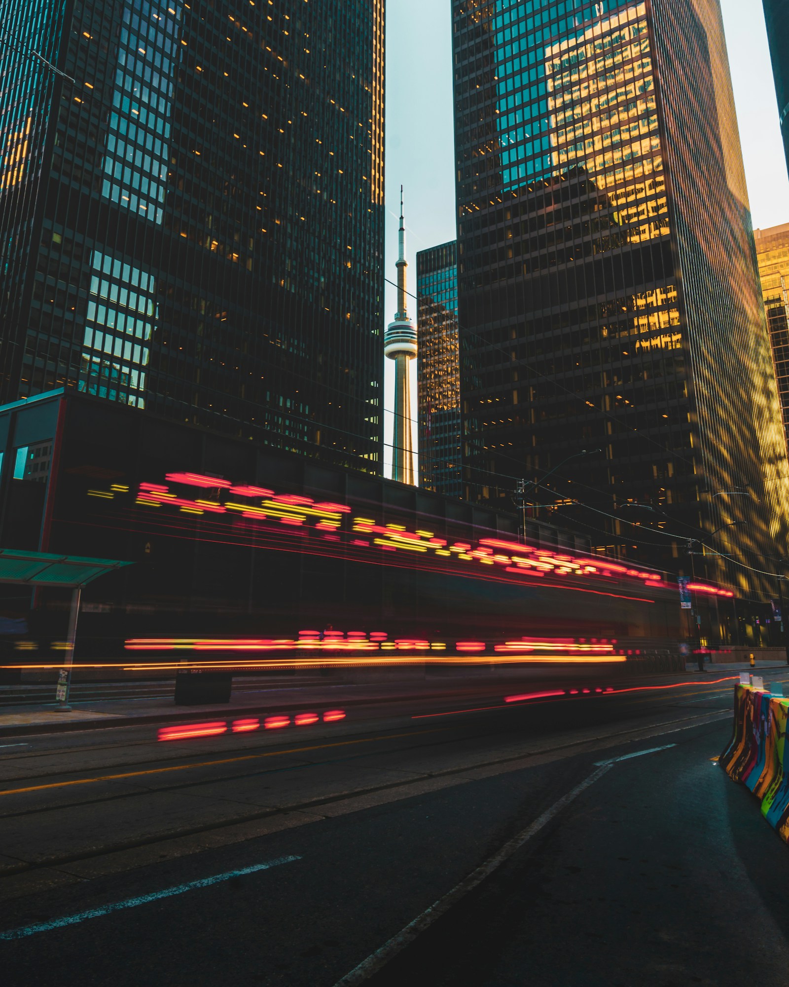 Blurred tram light trails on a downtown street between illuminated office towers at dusk, a tower silhouetted between them
