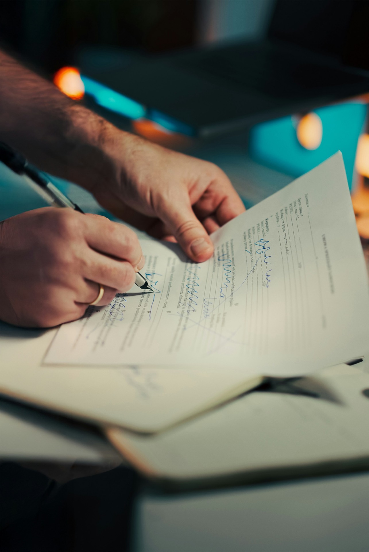 Close-up of a hand signing a document with a fountain pen on a desk, an open notebook visible beneath it