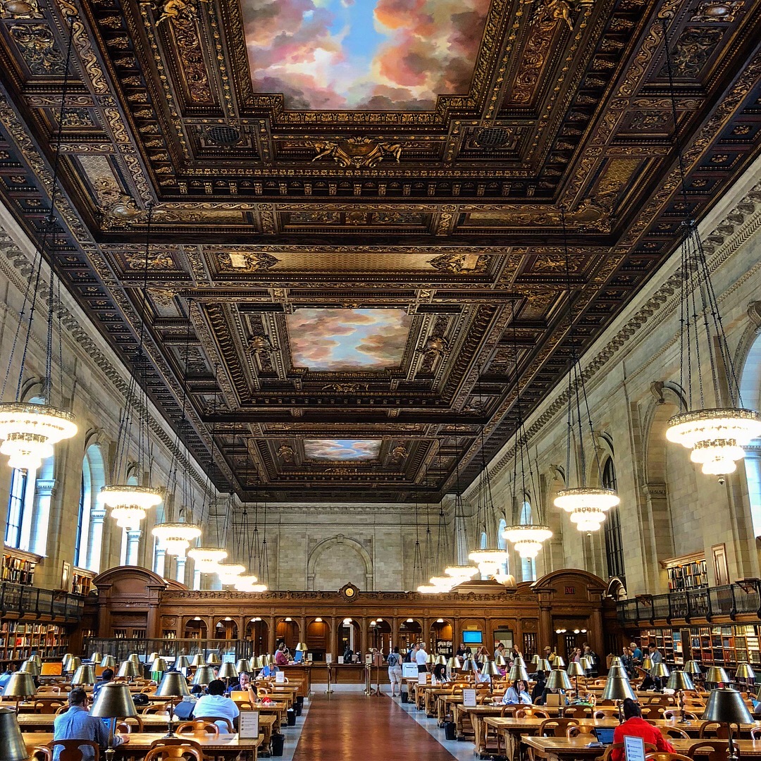 A quiet reading room with wooden desks and warm lamplight, an empty chair pulled up to an open notebook